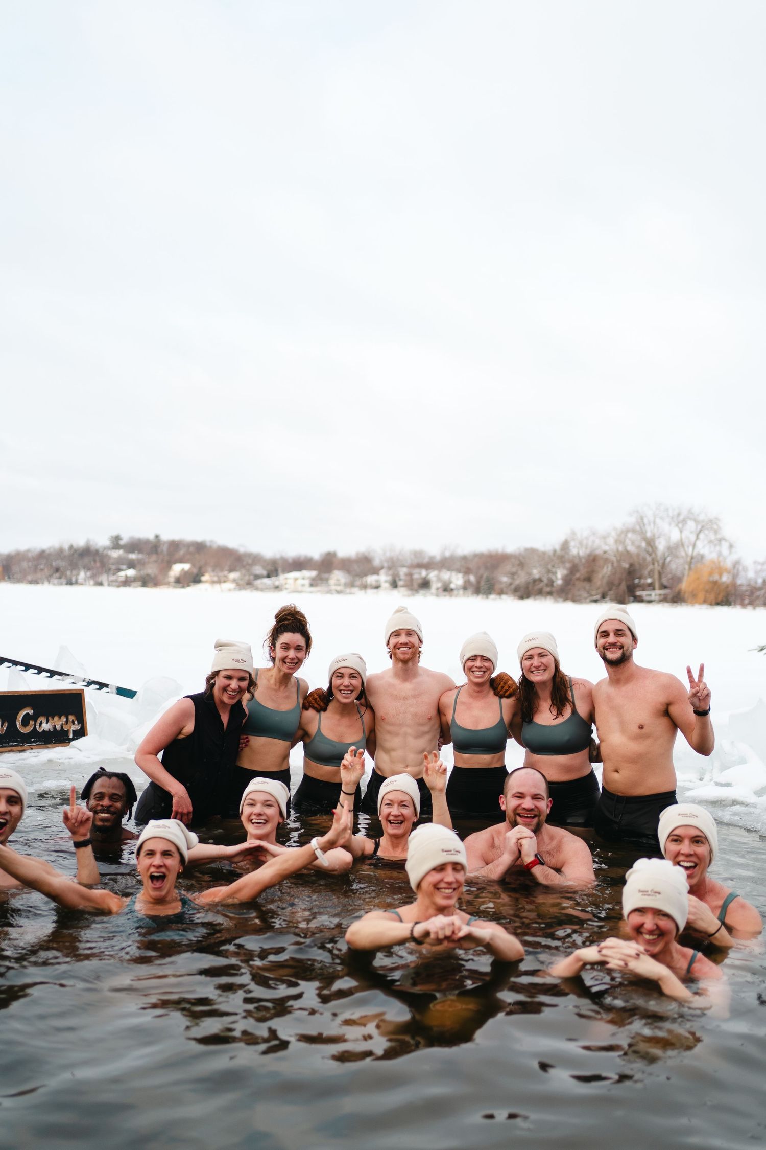 Group of winter swimmers enjoying an icy dip in a frozen lake with snow-covered landscape in the background.