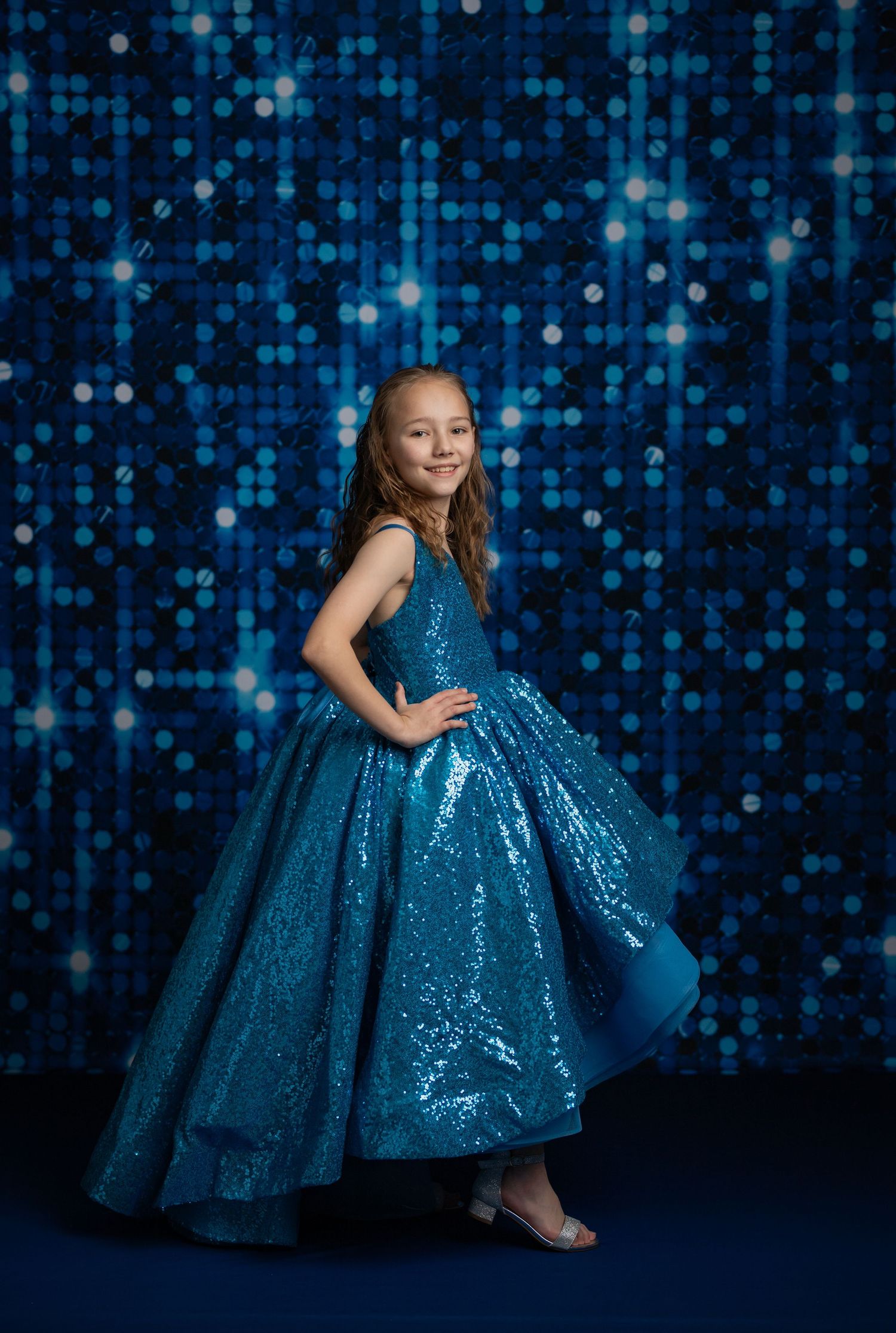 Child in flowing ice blue gown poses in magical winter wonderland scene with frozen castle backdrop and snowy stairs.