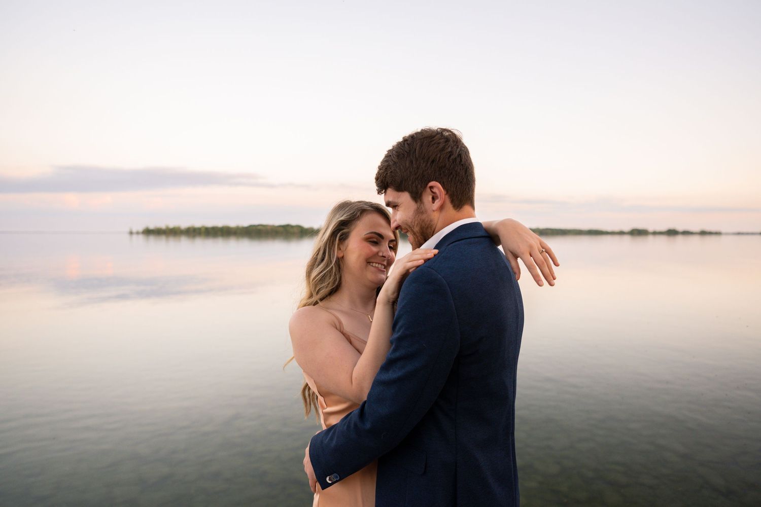 Couple in wedding attire walking together on green lawn at sunset.