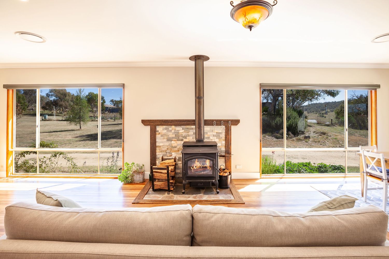 A cozy living room features a wood-burning fire place centered between large windows with scenic countryside views.