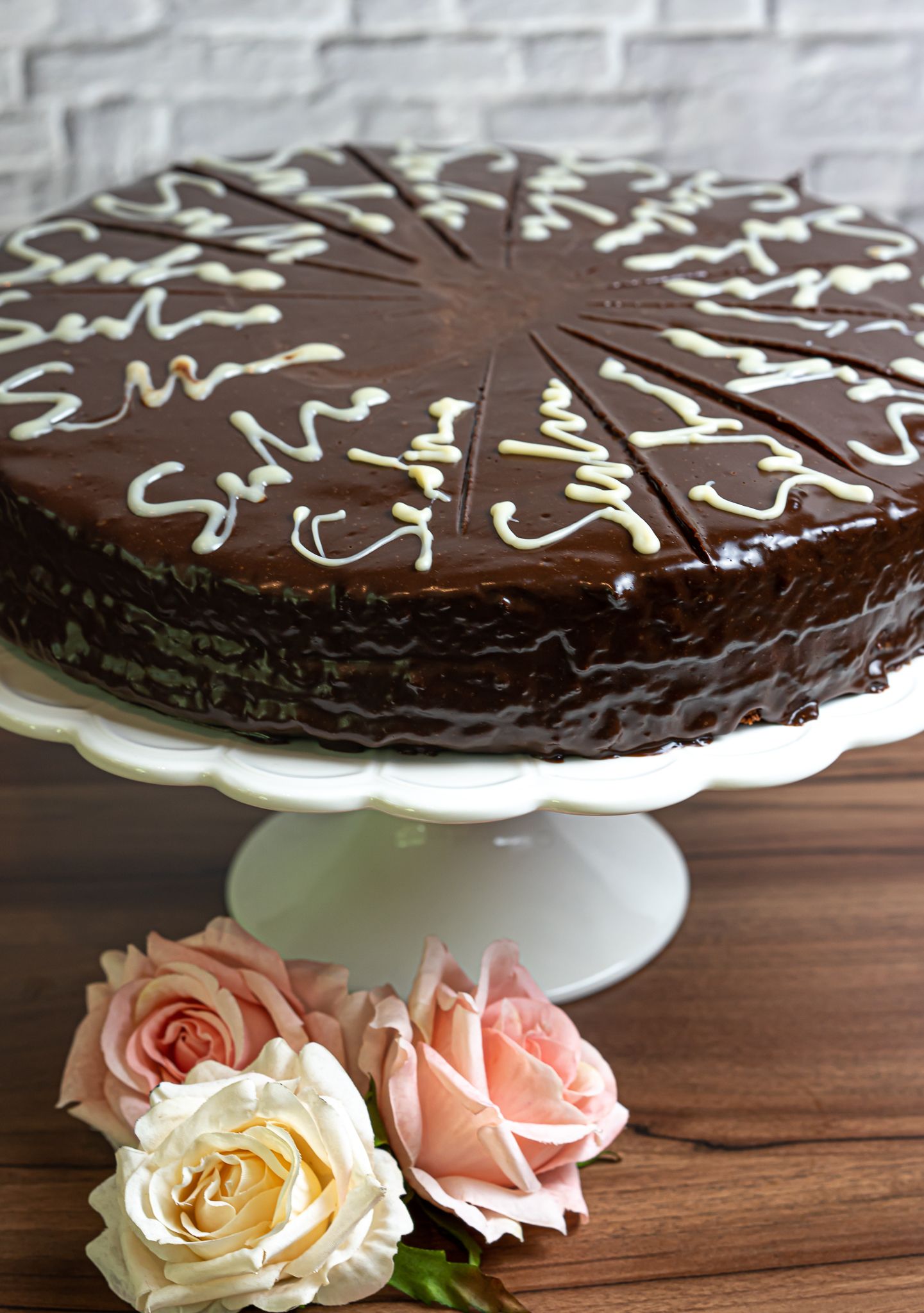 Foodfotografie - Chocolate cake with white icing decorations on a cake stand with fresh roses.