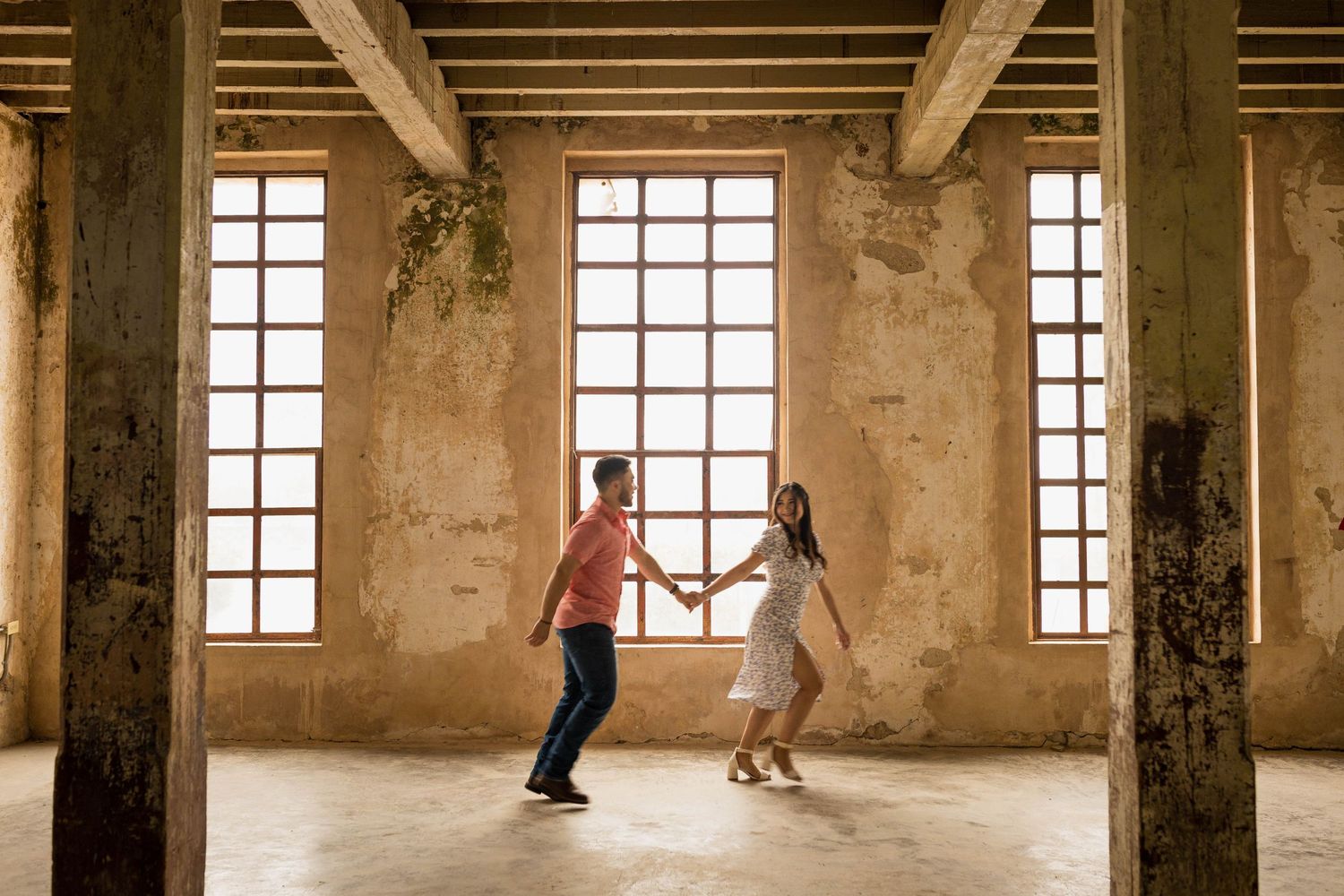 A couple dancing together in an industrial style room with large windows and exposed beams.