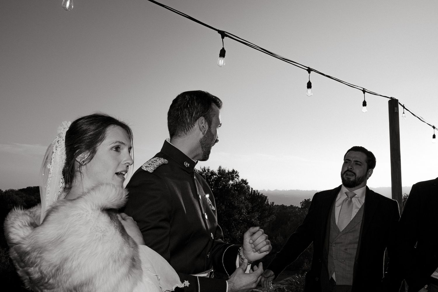 Outdoor celebration gathering at sunset with string lights overhead.