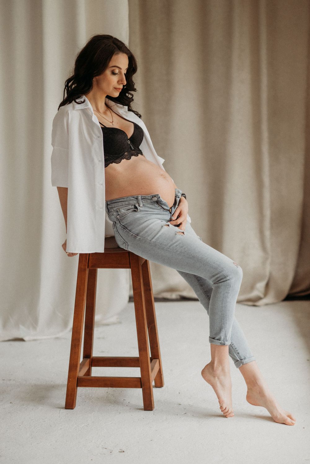 Artistic poses on wooden stool against neutral curtain backdrop.
