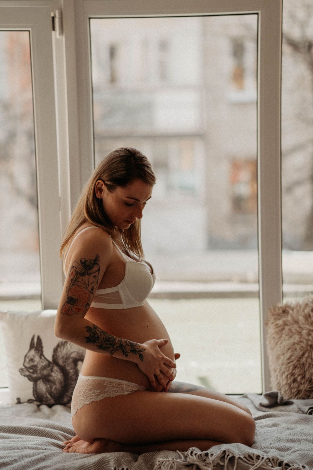 Intimate maternity boudoir photo by window with natural lighting.