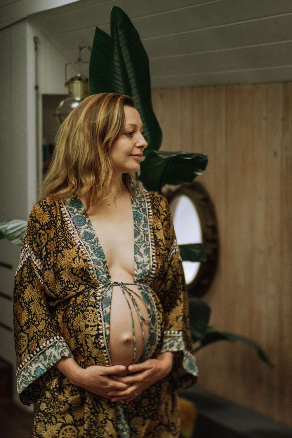 Indoor maternity session features a patterned vintage-style robe in warm lighting.