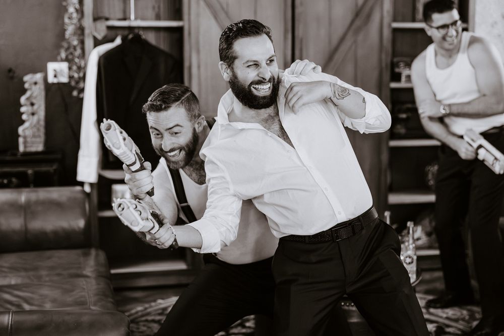 Groomsmen laughing and joking around in black and white photo during wedding preparations.