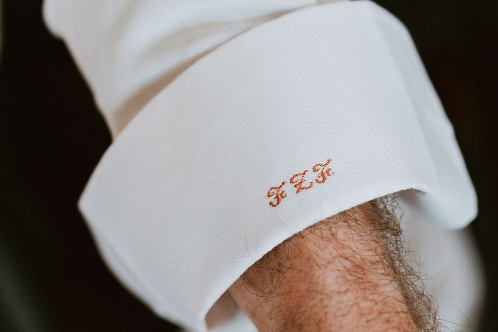 Close-up of white dress shirt cuff with elegant red monogram embroidery initials.