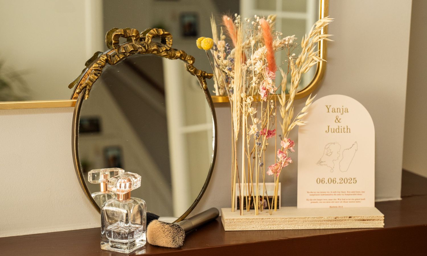 Een decoratief trouwbord met gedroogde bloemen en een gouden spiegel op een dressoir.