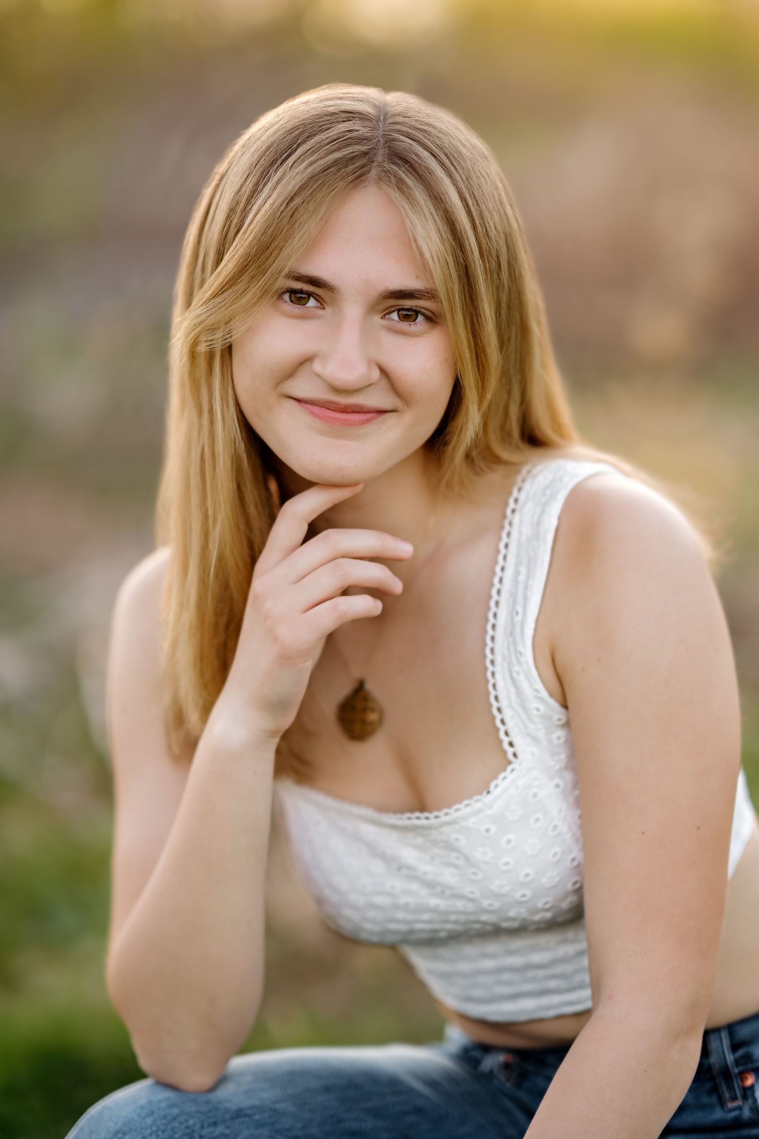 Young blonde woman in white lace crop top and jeans smiling outdoors in golden hour light.