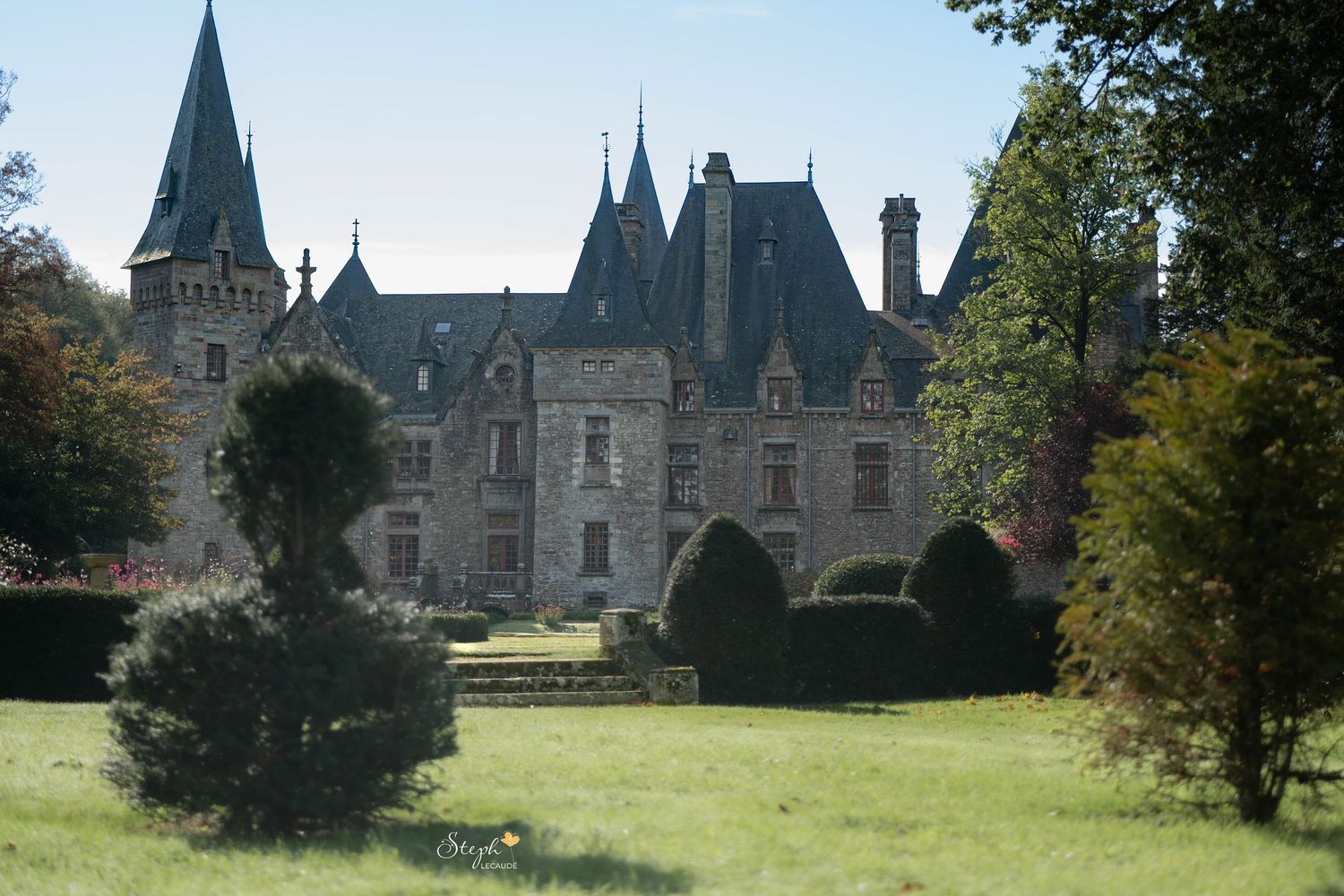 Château français historique doté de tourelles pointues, entouré de haies soigneusement entretenues et d'une pelouse verdoyante.