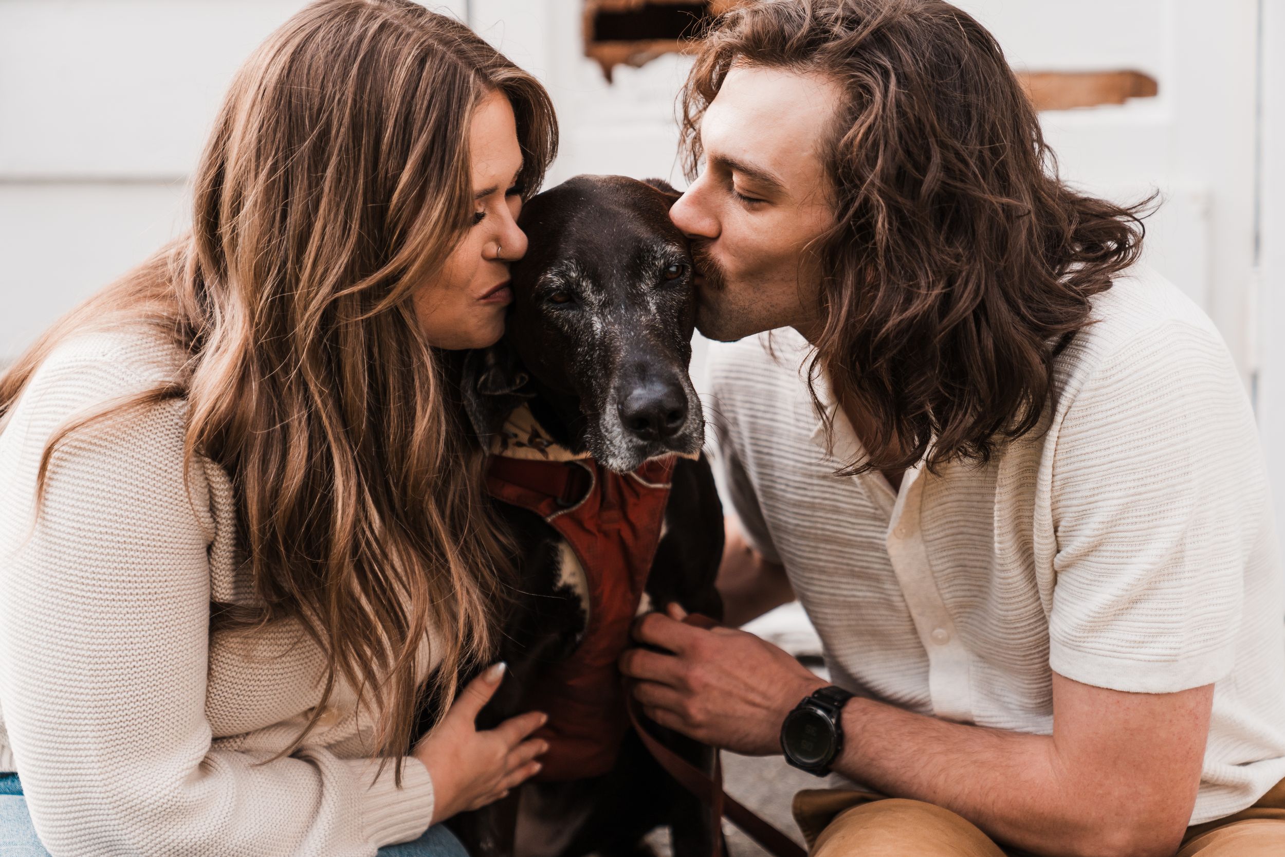 Couple affectionately nuzzling their black dog between them while sitting close together outdoors. engagement photoshoot discovery park