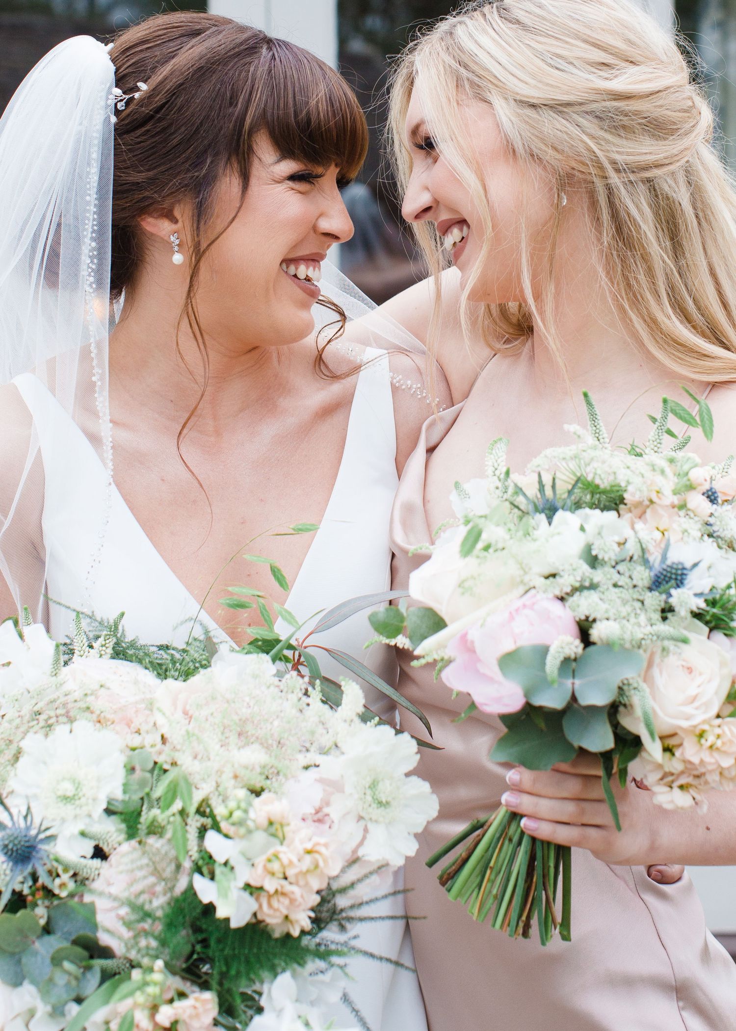 Bride and bridesmaid smiling at each other holding elegant white and pink floral bouquets on wedding day at The Prince George Hotel, NS