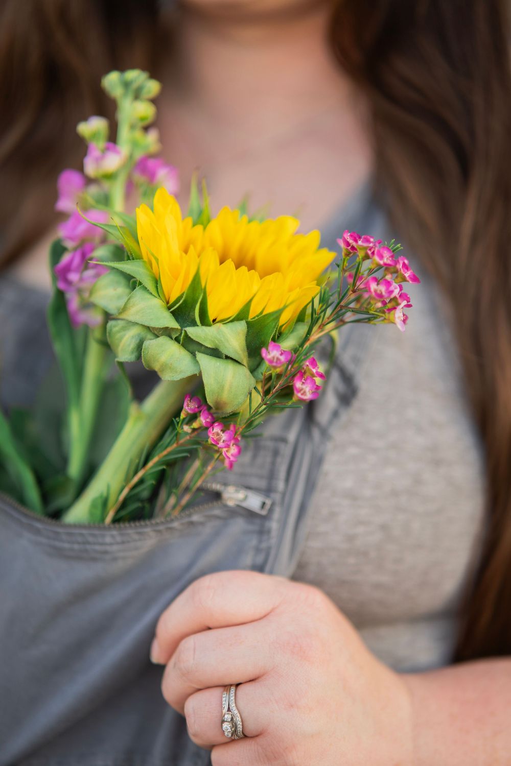 Close-up of woman holding sunflower and pink wildflower bouquet with silver ring on finger.