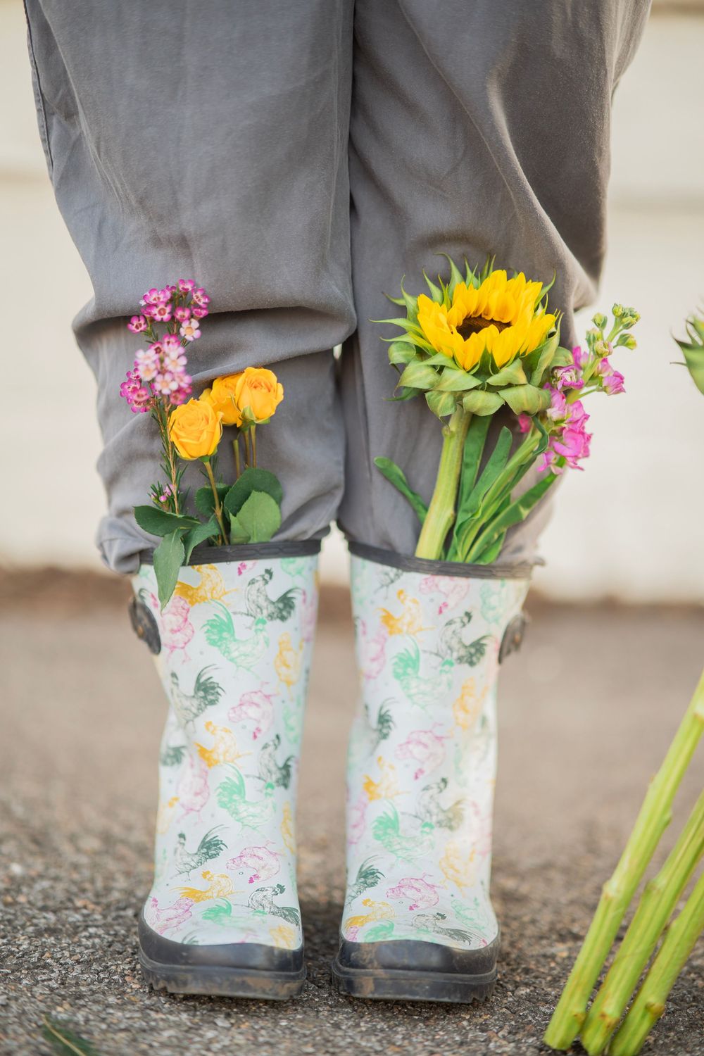 Floral rubber boots stuffed with sunflowers, roses, and colorful spring blooms on pavement.