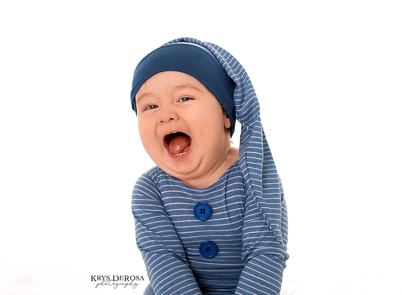 Laughing baby in blue striped onesie and navy nightcap poses against white background in professional photo.