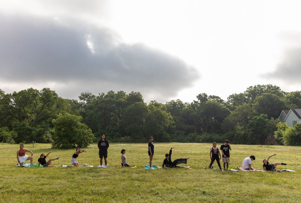 Group of people practicing yoga outdoors in a large green park field.