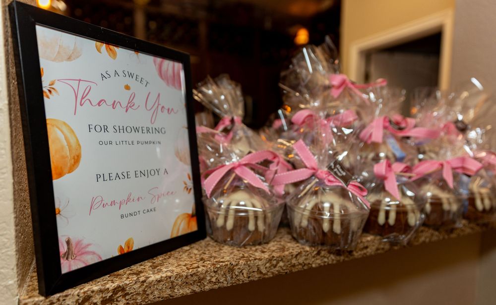 Baby shower favor table with chocolate-dipped cake pops tied with pink ribbons and a pumpkin-themed thank you sign.