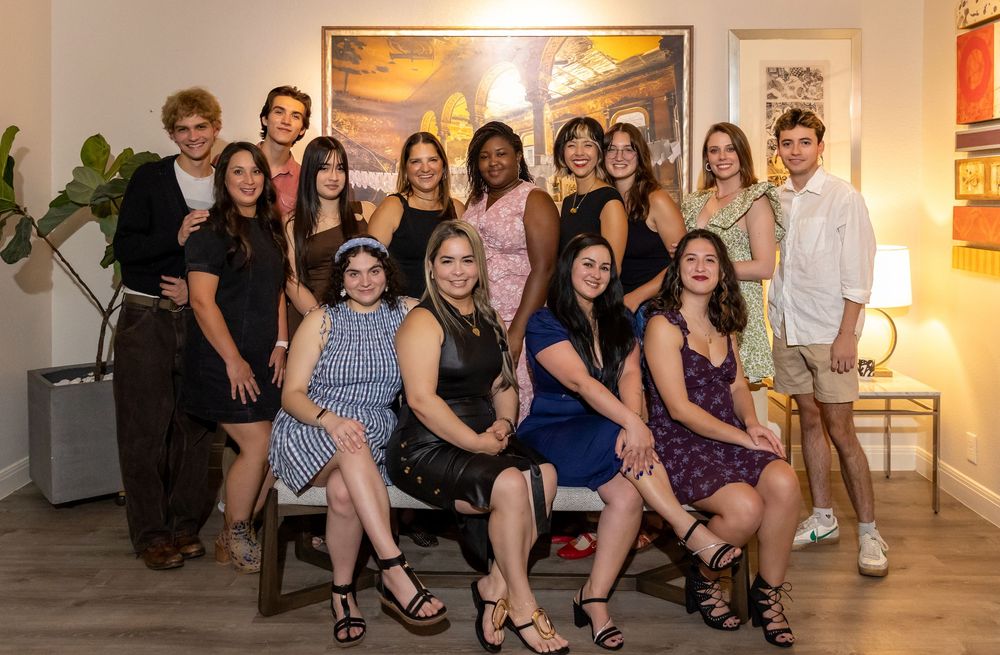 Group of smiling young adults posing together indoors at a formal gathering or celebration event.