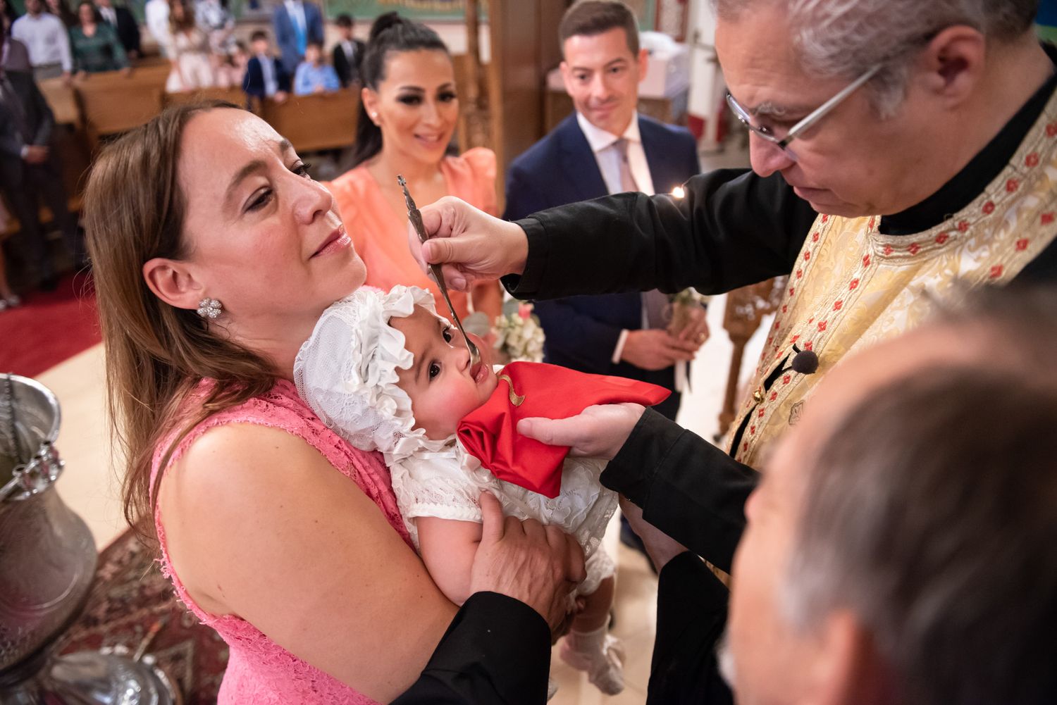 Orthodox priest performing anointing rite on baby during christening while godmother holds infant.