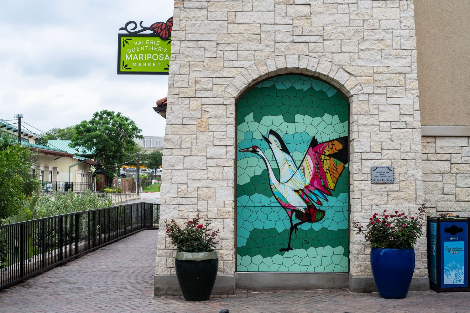 Colorful mosaic mural of a crane on a green door at Mariposa Garden Center, framed by stone walls and potted plants.