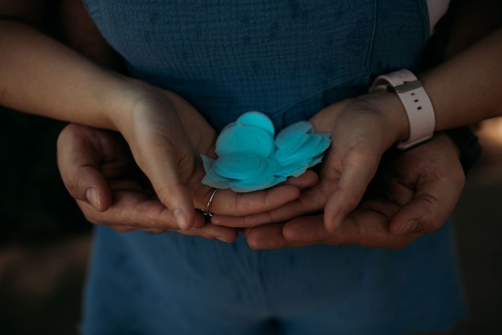 Hands gently holding turquoise blue confetti or paper pieces against a dark background.