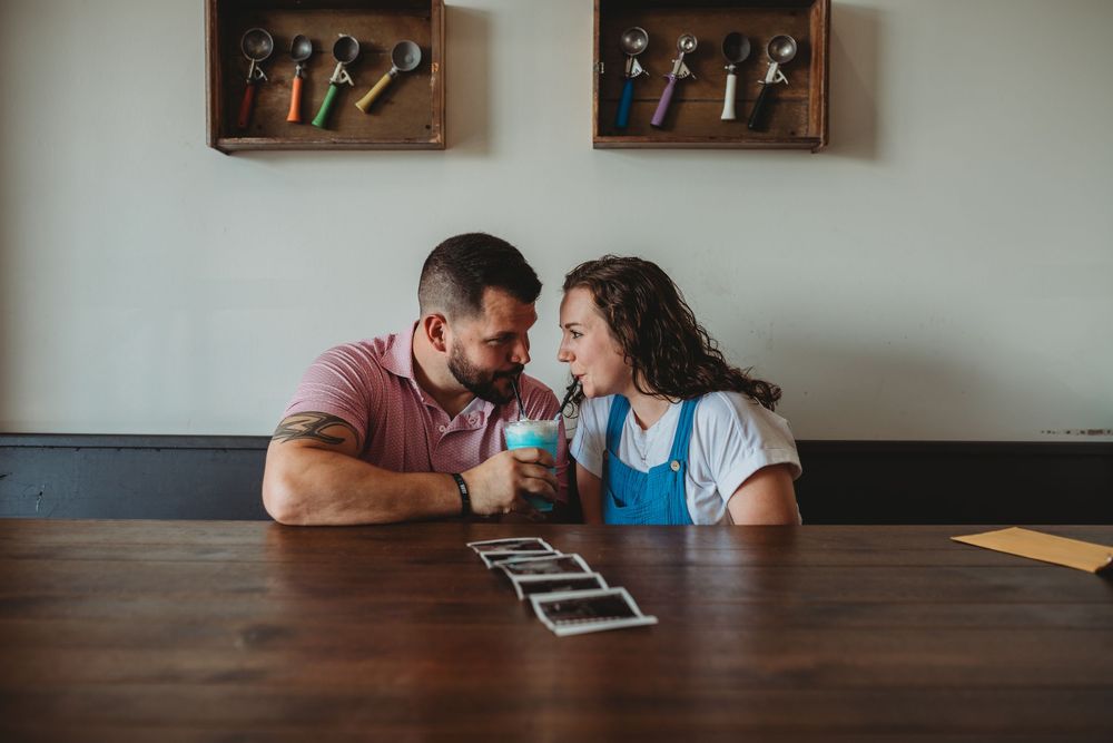A couple shares an intimate moment while sitting at a wooden table in a minimalist dining space.