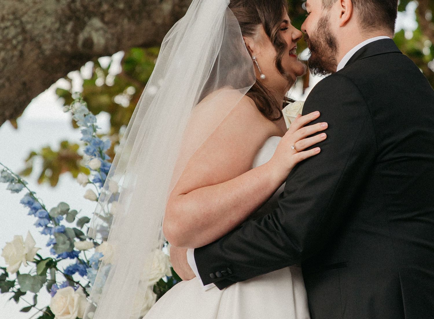 Groom in white suit and cowboy hat sees bride in lace wedding dress holding bouquet during outdoor first look.