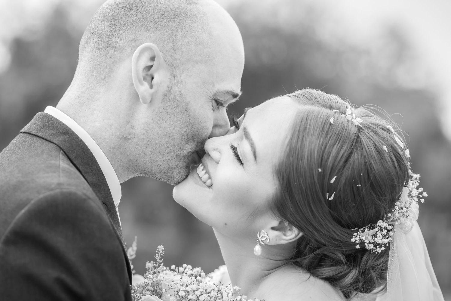 Black and white wedding photo of a smiling bride and groom sharing a tender kiss outdoors.