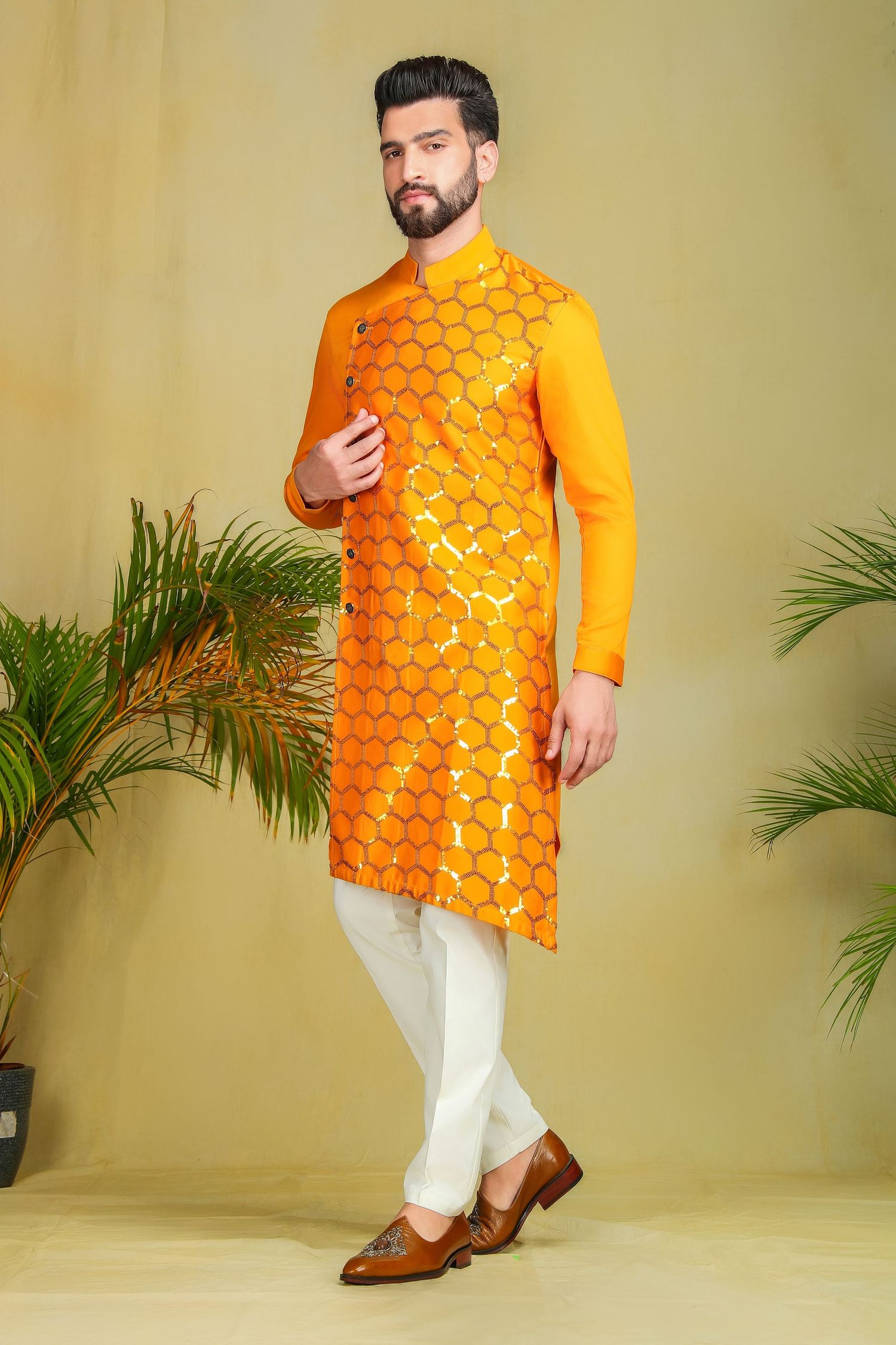 Man wearing orange embroidered kurta with white churidar and brown loafers, traditional Indian festive ethnic wear.