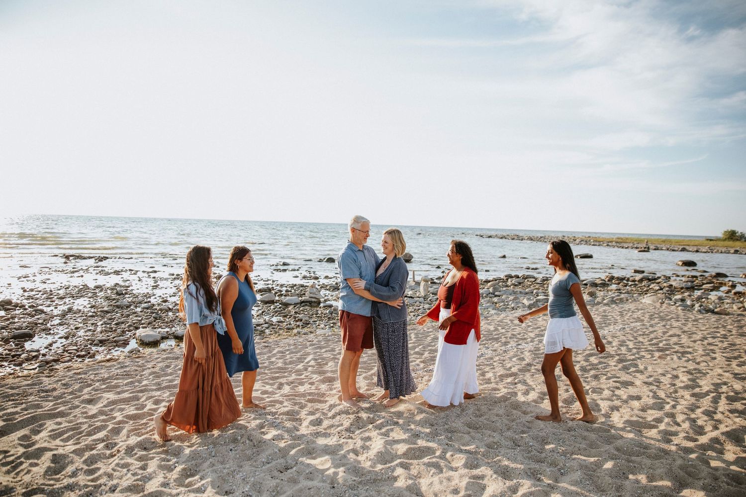 Family group smiling and socializing on a sunny sandy beach near the ocean on a bright clear day.