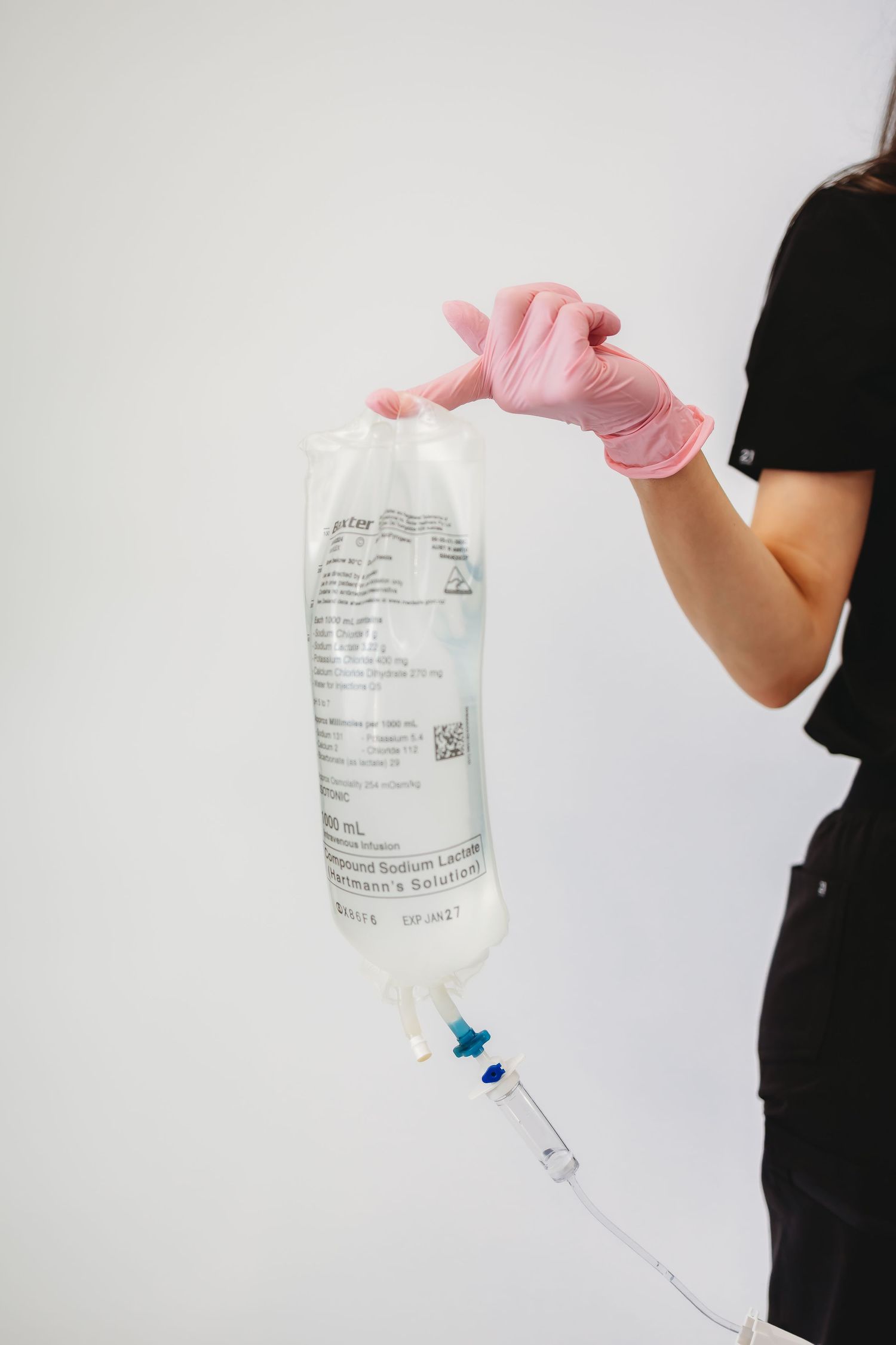 Healthcare worker in pink gloves holding a Lactated Ringer's IV saline bag with tubing against white background.