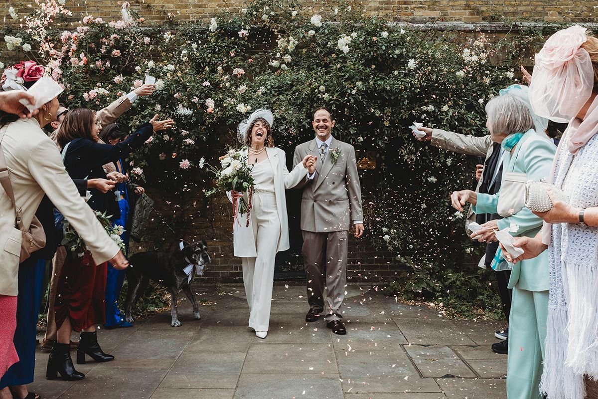 Newlywed couple walks through confetti shower surrounded by cheering guests at an elegant outdoor wedding ceremony.
