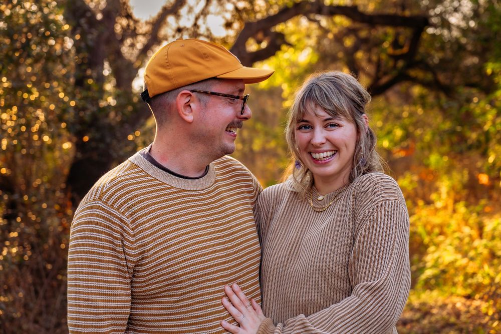 A genuine, un-staged lifestyle portrait of a smiling couple during an autumn session in a natural outdoor setting.
