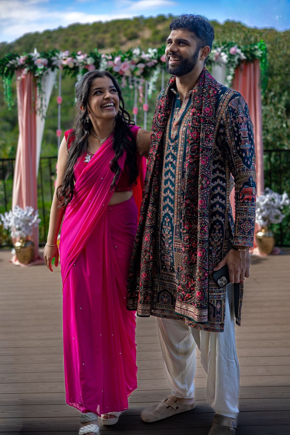 A vibrant outdoor wedding portrait of a couple in traditional attire standing under a floral archway in Austin, Texas.