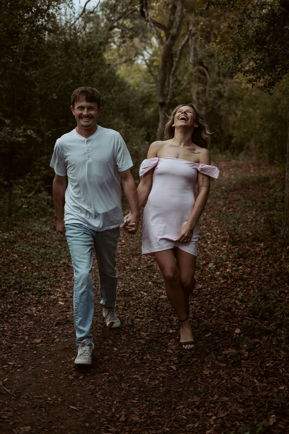 A natural, un-staged lifestyle portrait of a couple walking through a wooded trail during a sunset session in Buda, Texas.