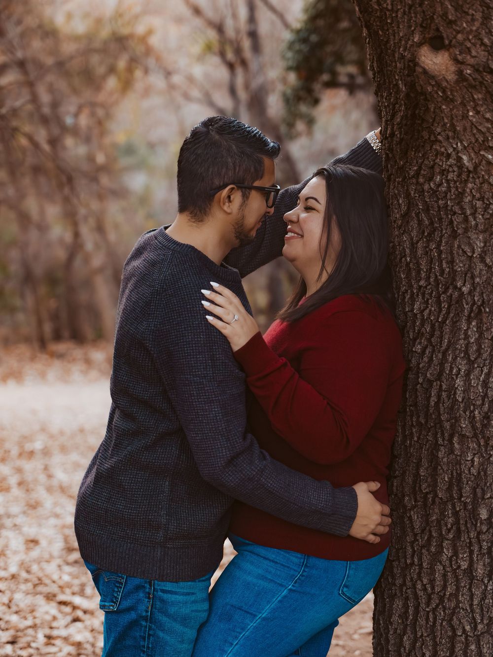 Intimate "Love Stories" portrait of a couple embracing against a tree in a wooded Buda, Texas setting.