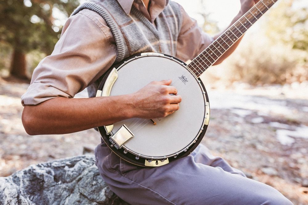 Man playing a banjo outdoors, strumming strings while seated on a rock in the mountains near yucaipa ca
