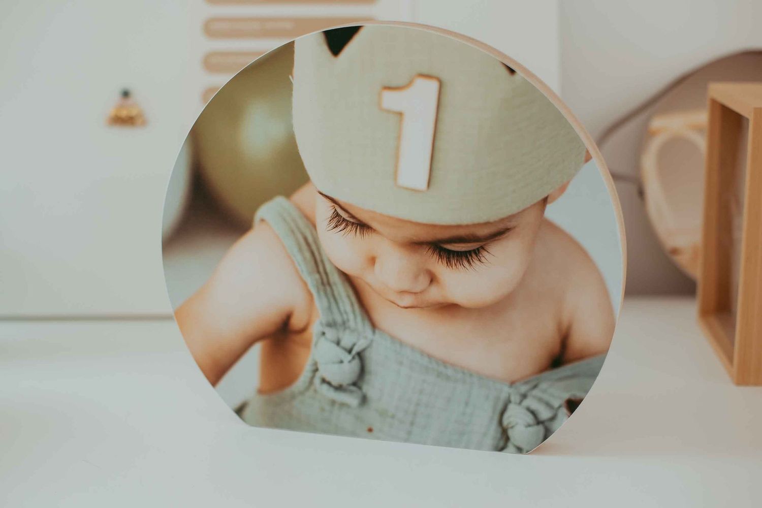 A baby wearing a crown with the number 1 celebrates their first birthday in a soft, neutral-toned photo print.
