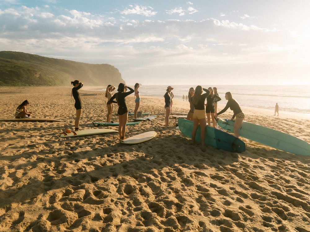 photo of 12 girls checking the surf at the beach in a circle in golden light on a group social surf with Sunlight Surfers Dudley Newcastle