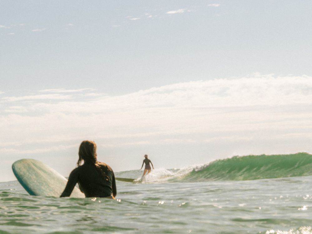 out of focus shot of a girl sitting on the surfboard in foreground on a group social surf with Sunlight Surfers Dudley Newcastle NSW