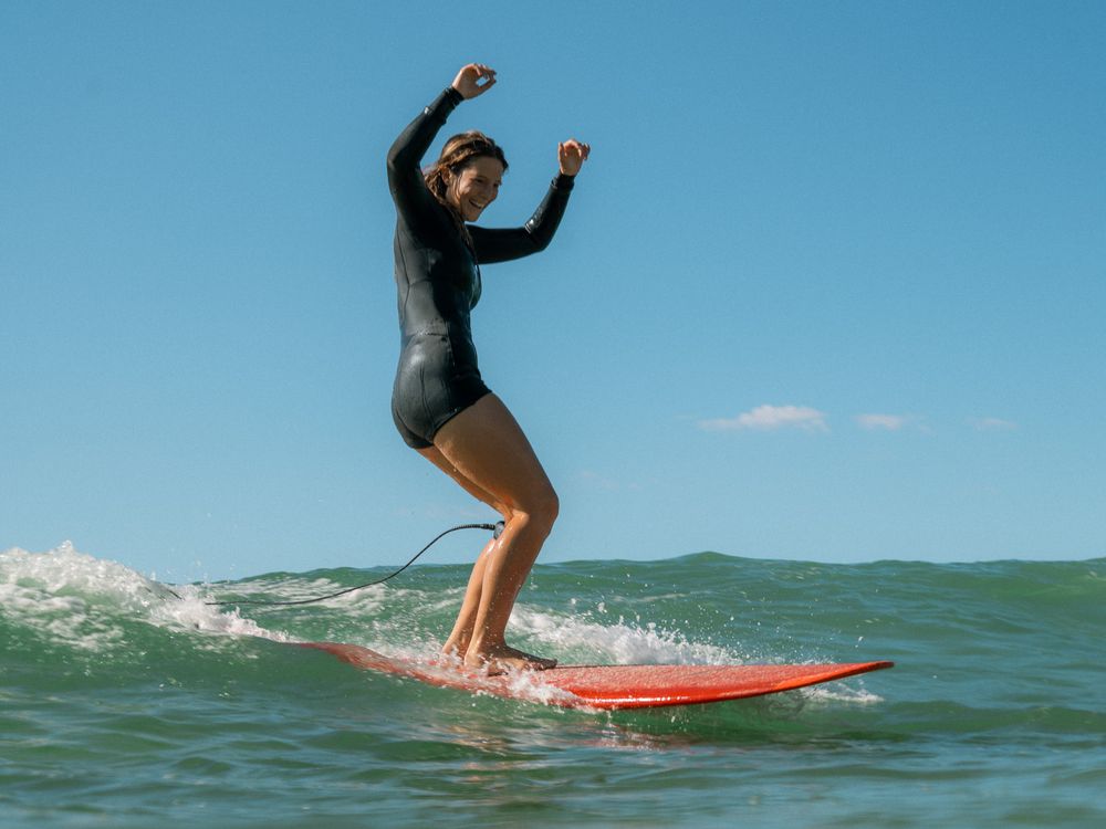 intermediate surfer with hands in the air laughing on a small wave on a group social surf with Sunlight Surfers Dudley Newcastle NSW