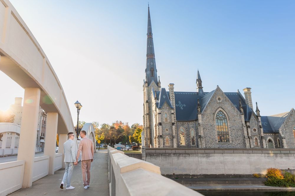 Groom and groom walk hand in hand over a bridge towards a church in downtown galt in Cambridge, Ontario.