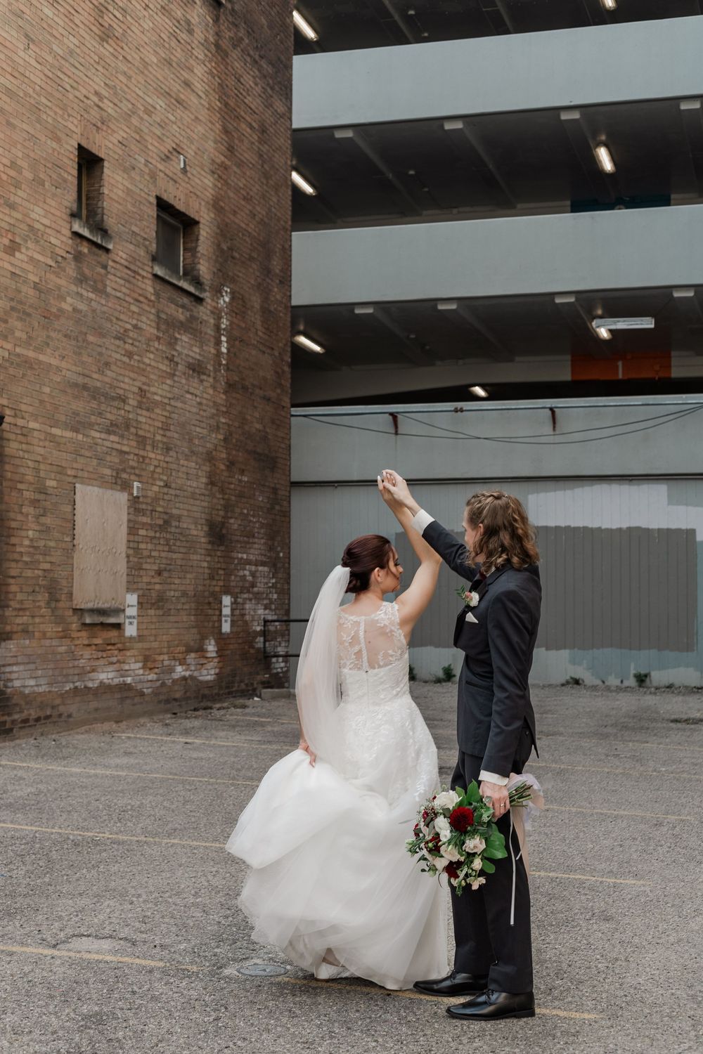 Groom twirls his bride while holding the flowers in an alley by The Walper Hotel in downtown Kitchener, Ontario.