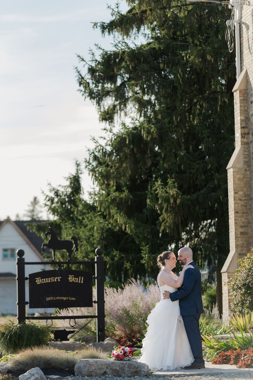 Bride and groom stand close to each other in front of Hauser Hall in St. Jacobs, Ontario.