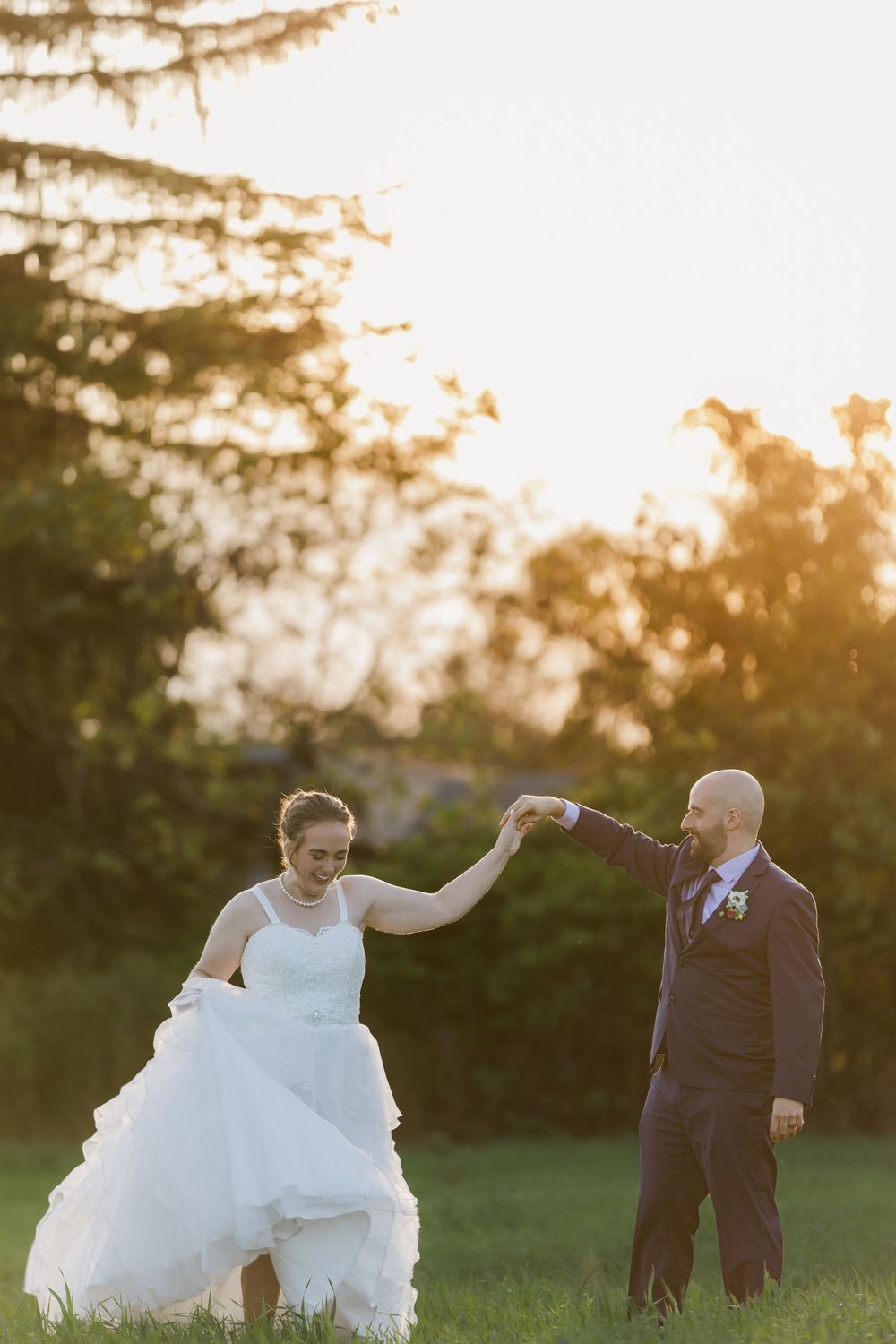 Groom twirls his bride in a green field during sunset behind hauser hall in St. Jacobs, Ontario.