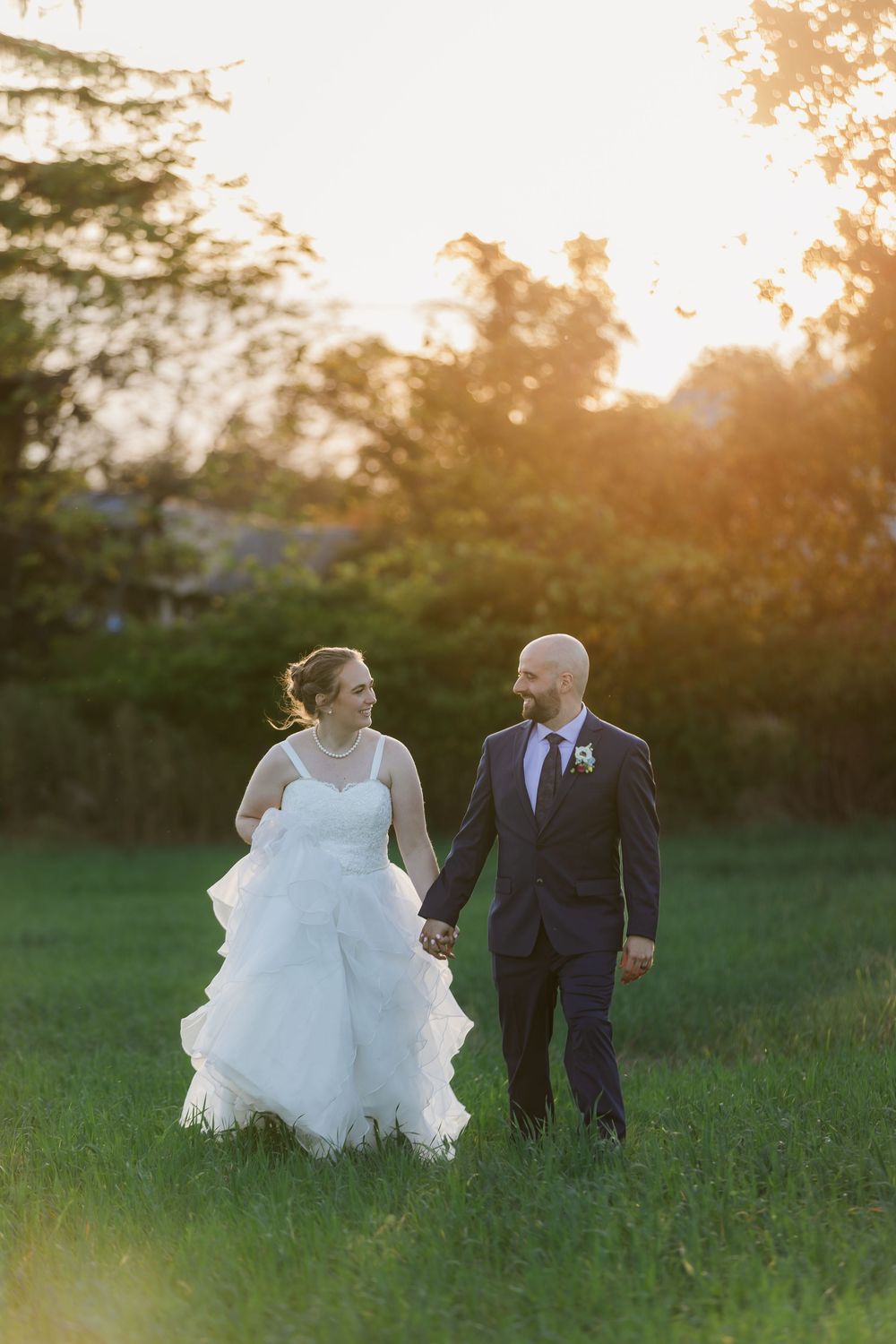 Bride and groom holding hands walking in a field during sunset at the back of hauser hall in St. Jacobs, Ontario.