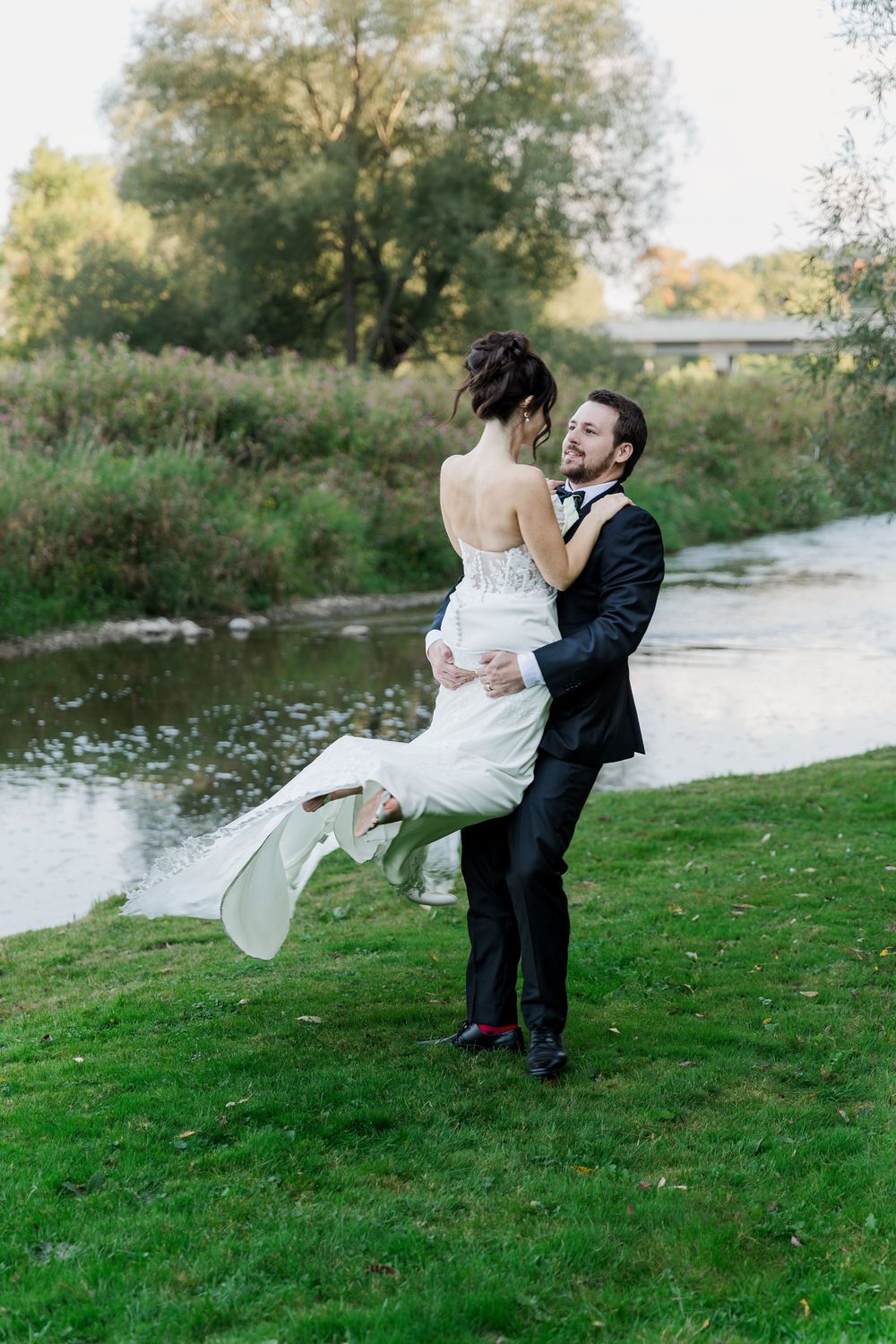 Groom picking up his bride and spinning her along the side of the grand river at the Wren House in St. Jacobs, Ontario.