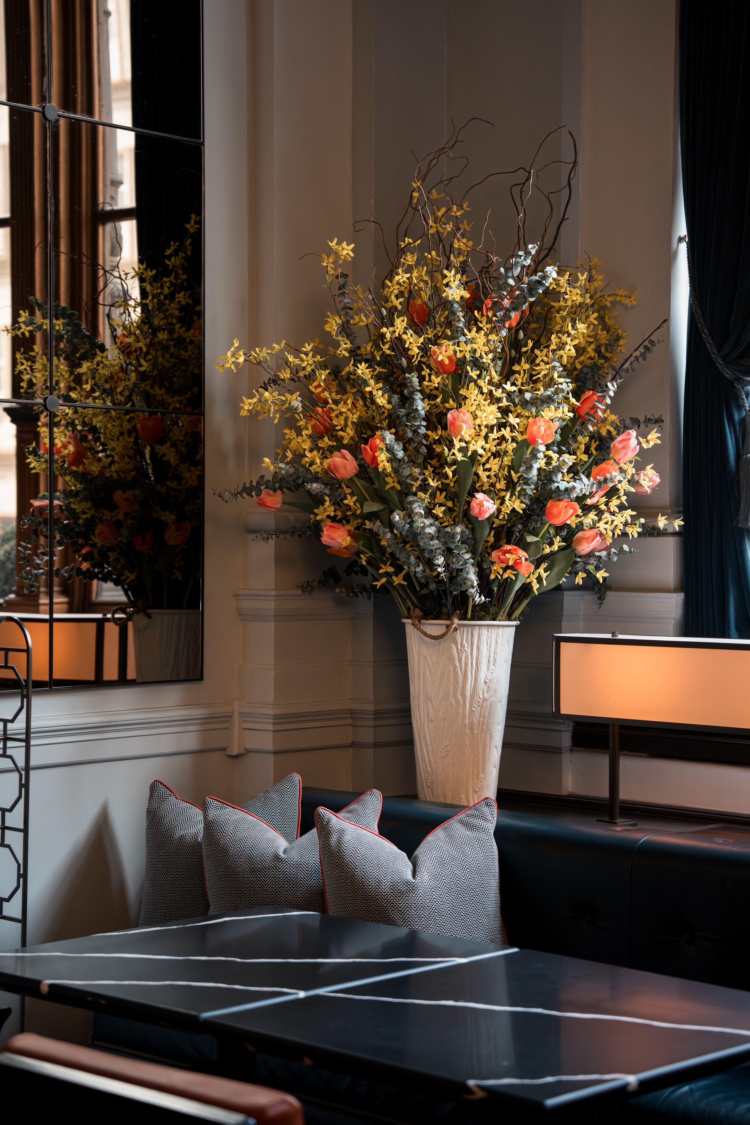 Elegant floral arrangement with pink roses and yellow blooms in a white vase on a dark marble table in a luxury interior.