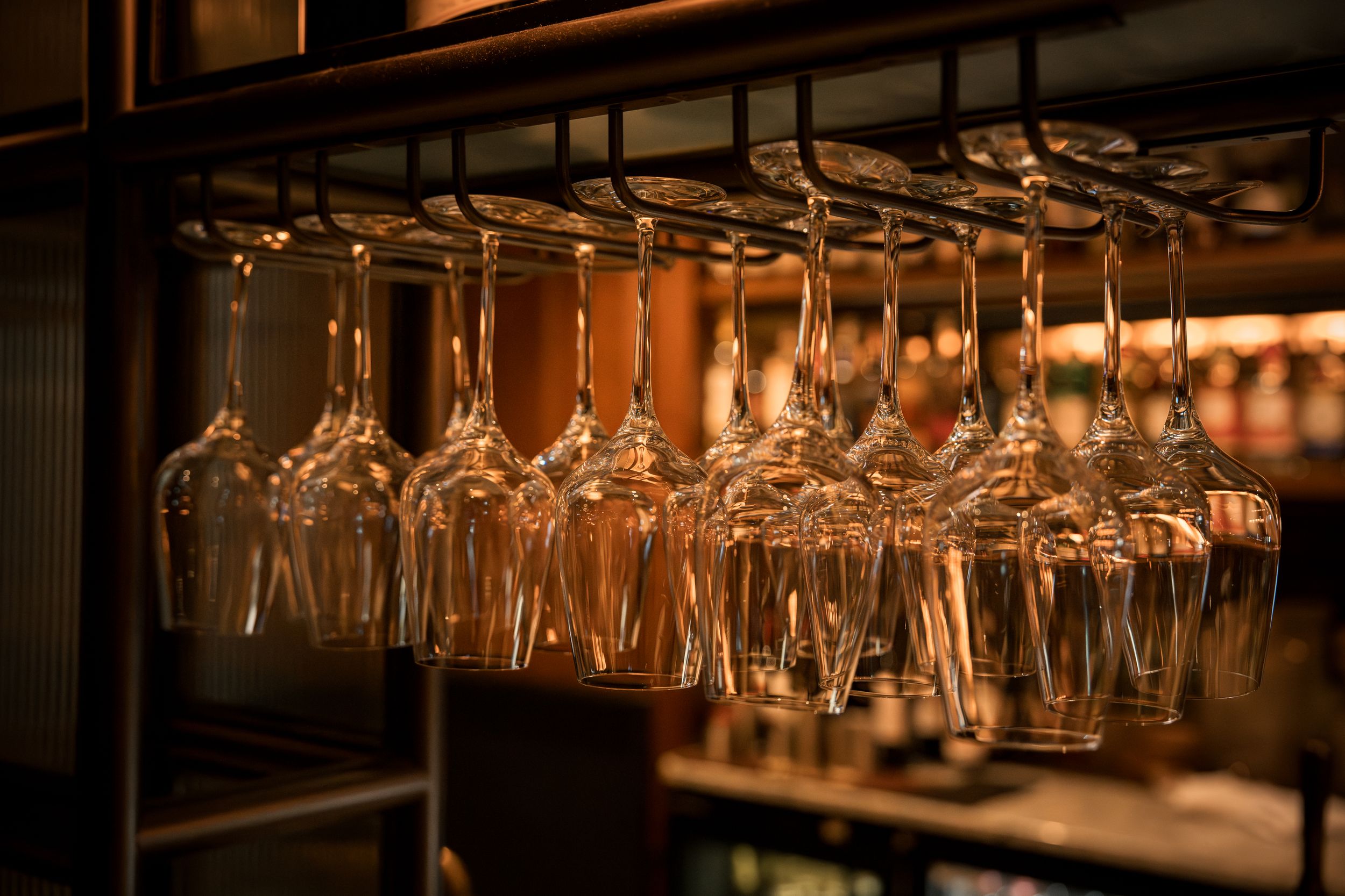 Crystal wine glasses hanging upside down on a metal rack in a warmly lit bar setting.